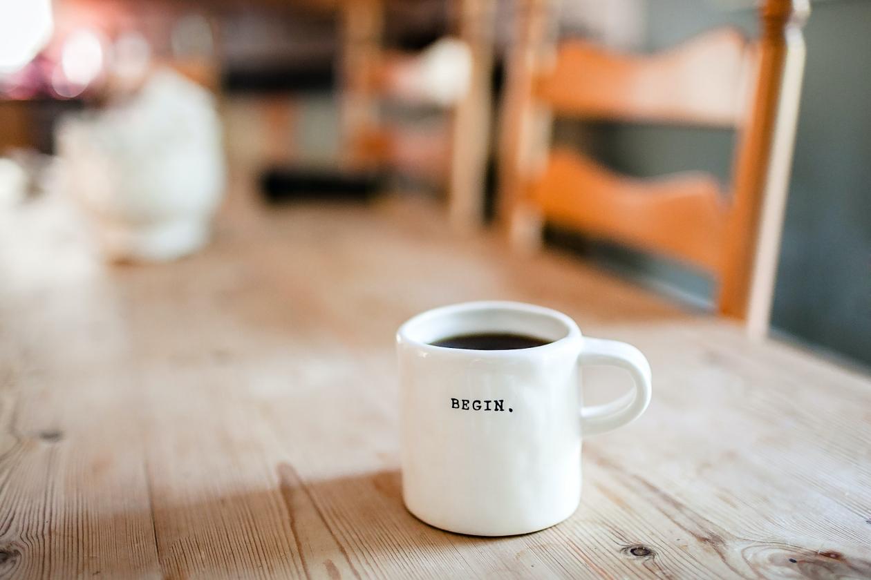 A coffee cup sitting on a dining room table with the word "begin" written on it.